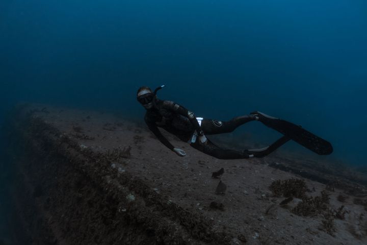 Scuba diver swimming near a submerged structure in deep blue water.