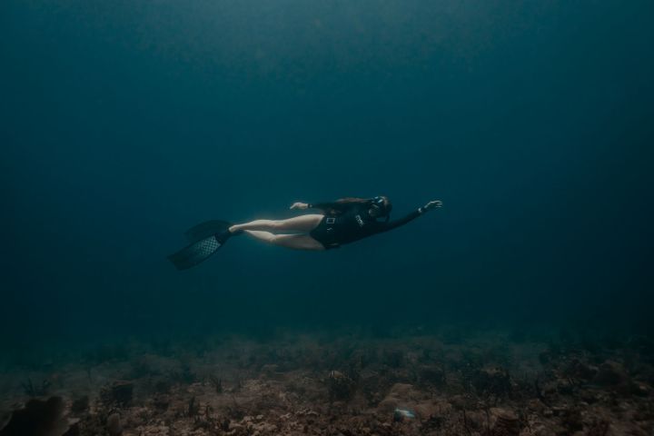 Person in diving gear swimming underwater over a coral reef.