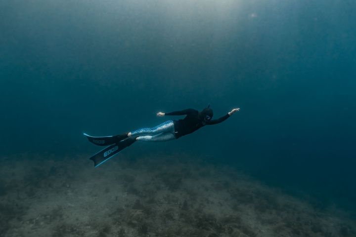 Person in wetsuit and fins diving underwater over seabed.