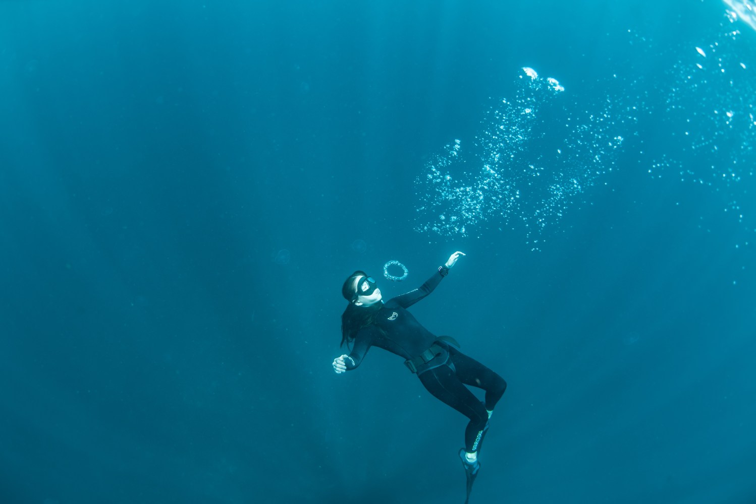 A diver in a wetsuit blowing bubble rings in blue ocean water.