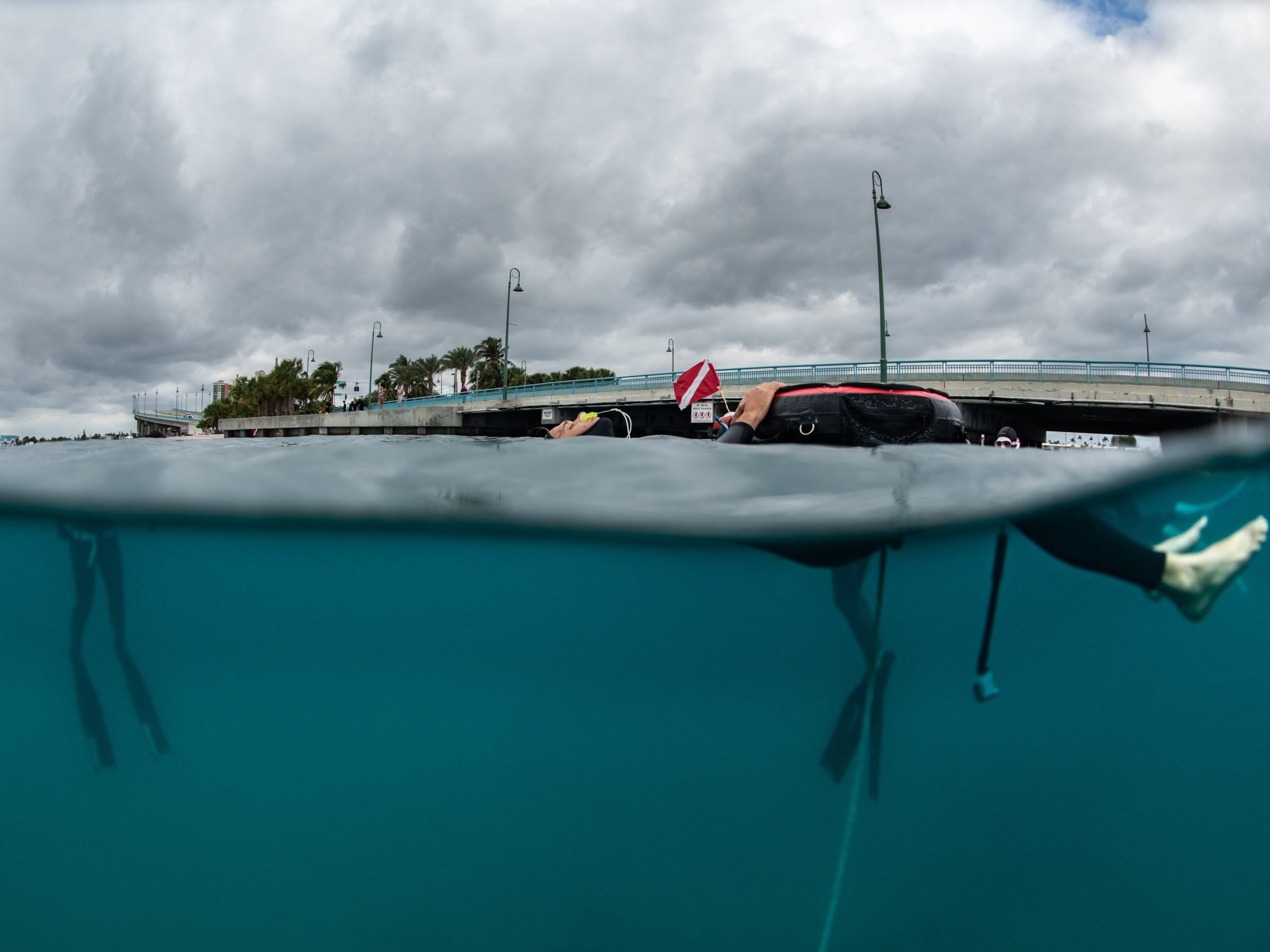Split view of snorkeler by a bridge with cloudy sky above and water below.