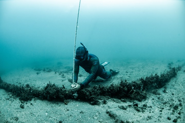 Underwater diver holding a rope near the ocean floor in clear blue water.