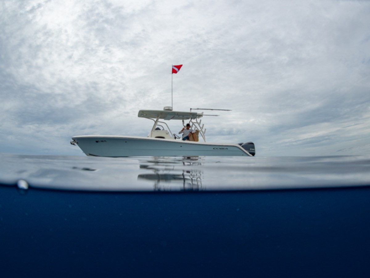 Boat with dive flag on calm sea, cloudy sky reflected in water.