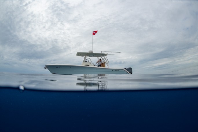 Boat with dive flag on calm sea, cloudy sky reflected in water.