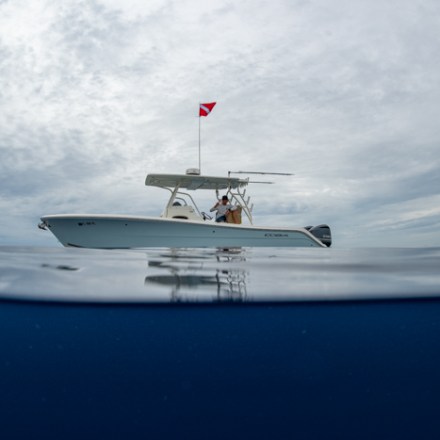 Boat with dive flag on calm sea, cloudy sky reflected in water.