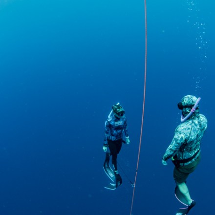 Two divers in wetsuits floating underwater beside a guide rope in deep blue ocean.
