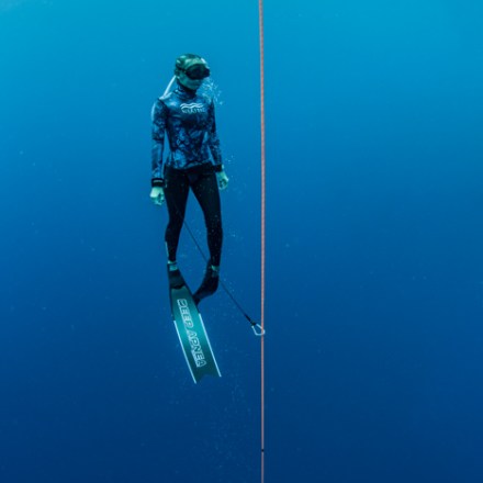 Diver with fins and snorkel floating vertically beside a rope in deep blue water.