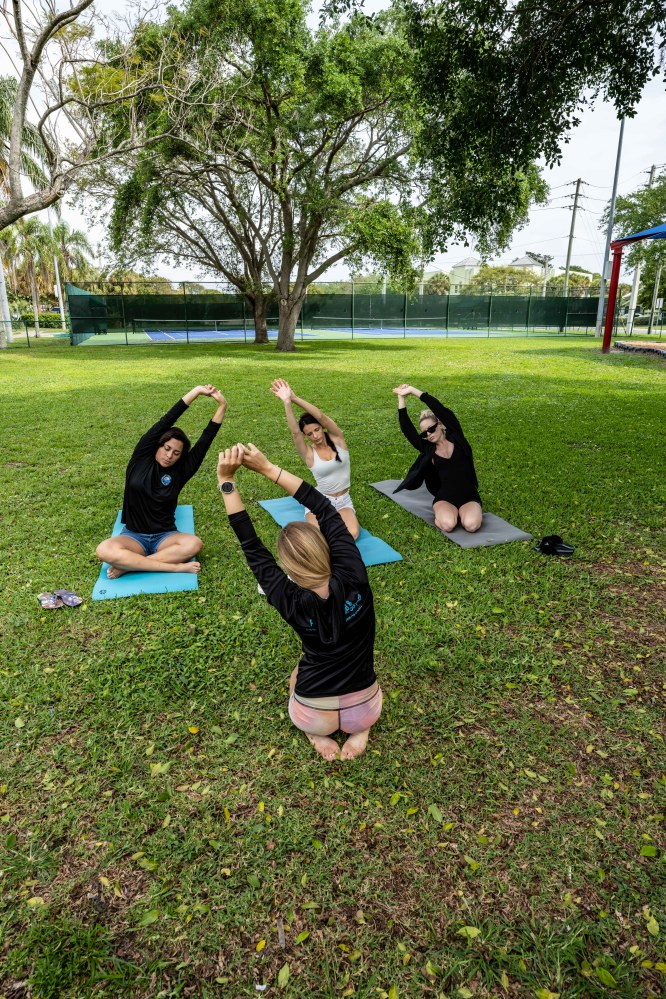 Four people doing yoga on mats in a park with trees in the background.