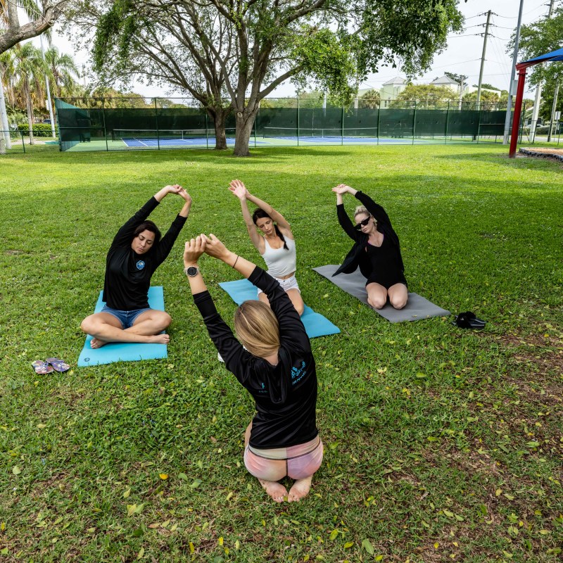 Four people doing yoga on mats in a park with trees in the background.
