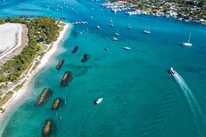 Aerial view of a coastal area with boats, clear blue water, sandy beaches, and green vegetation.