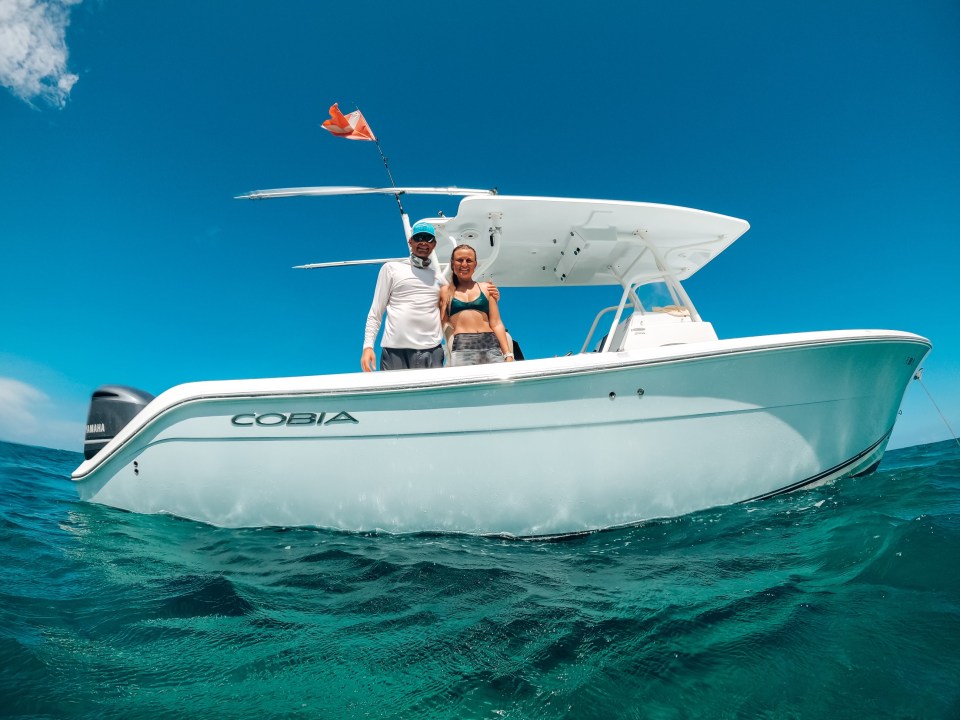 Two people standing on a white boat named COBIA in the ocean under a clear blue sky.