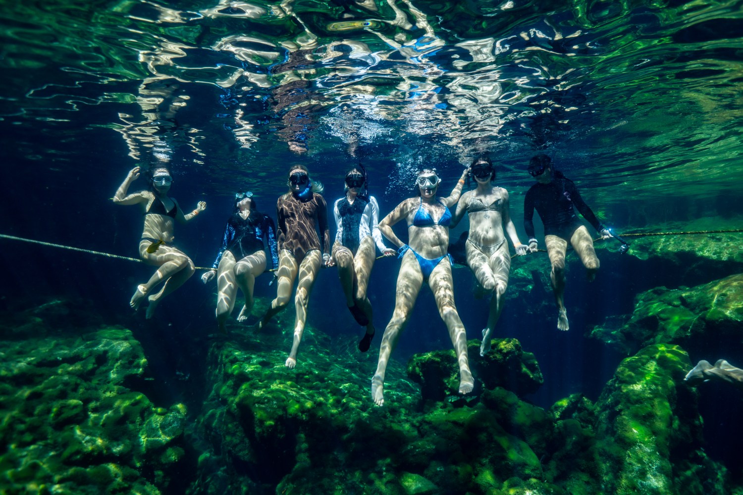 Seven people snorkeling underwater, floating above rocky sea floor.