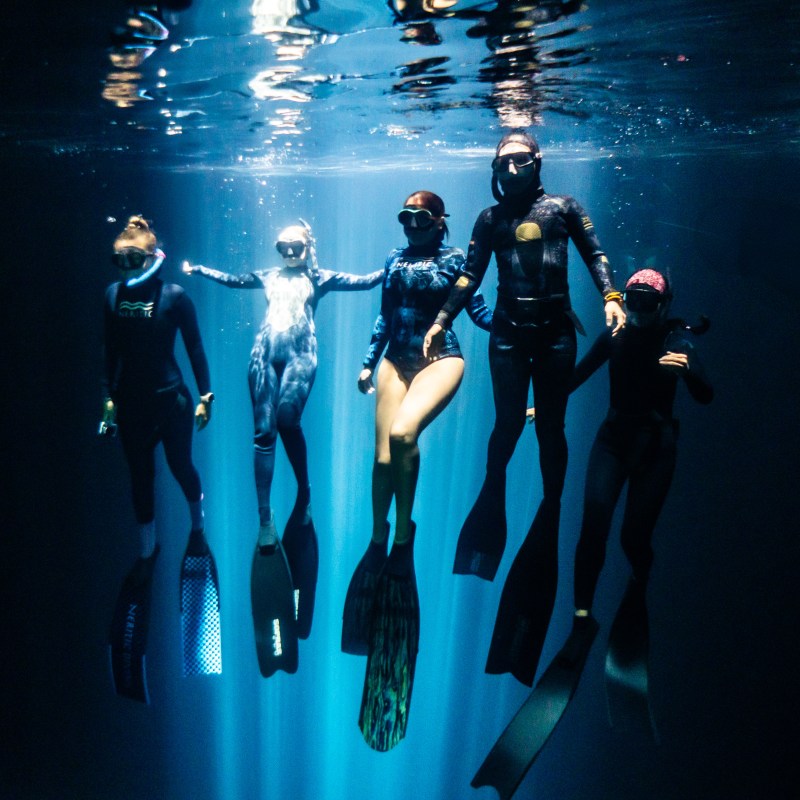 Five snorkelers underwater with fins, illuminated by light shafts.