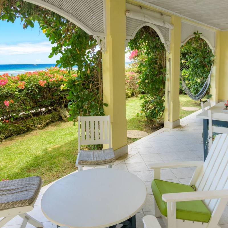 Outdoor patio with white chairs, hammock, and ocean view, surrounded by flowers and greenery.
