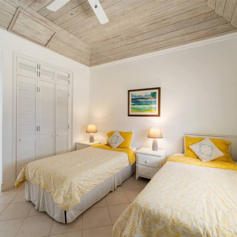 Bedroom with two beds, yellow bedding, and a painting above a nightstand; door and window visible.
