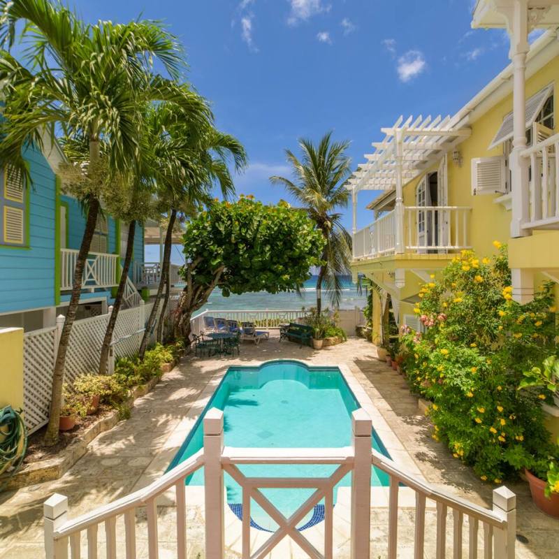 Tropical courtyard with a pool, bordered by colorful buildings and palm trees, leading to the ocean.