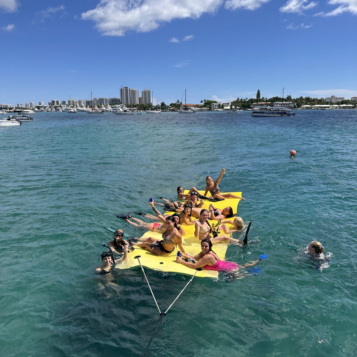 Group of people on a floating platform in the ocean, with a city skyline in the background.