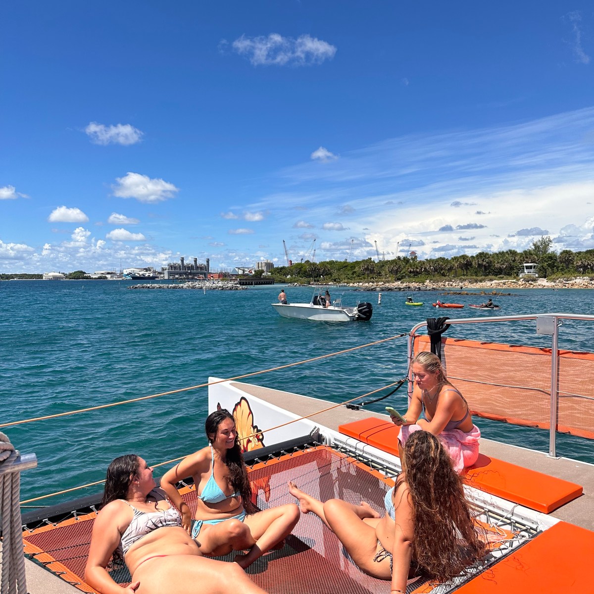 Four people relaxing on a boat's netting over water on a sunny day.