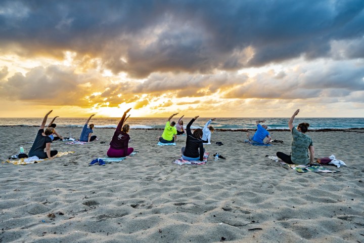 People doing yoga on a beach at sunrise with cloudy sky.
