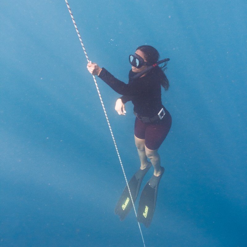 Person in diving gear ascending with rope underwater.