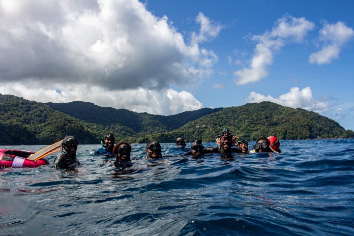 Group of snorkelers in the ocean with hills and cloudy sky in the background.