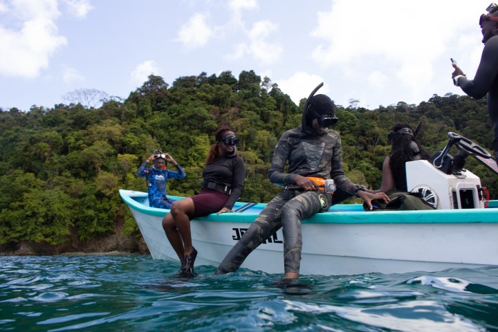 People in snorkeling gear on a boat near a forested island.