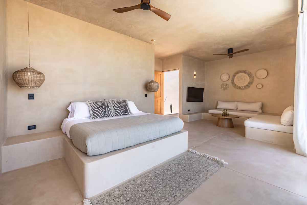 Minimalist bedroom with bed, seating, neutral tones, and ceiling fan.
