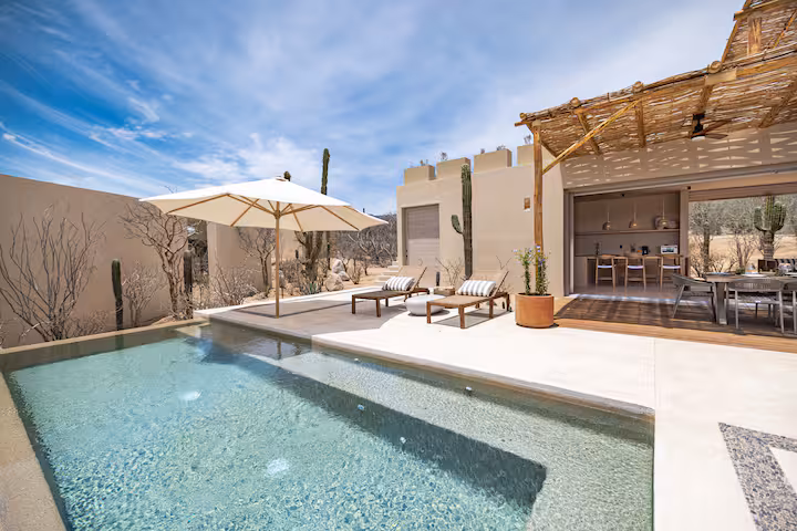 Modern patio with pool, sun loungers, umbrella, outdoor dining; desert landscape.