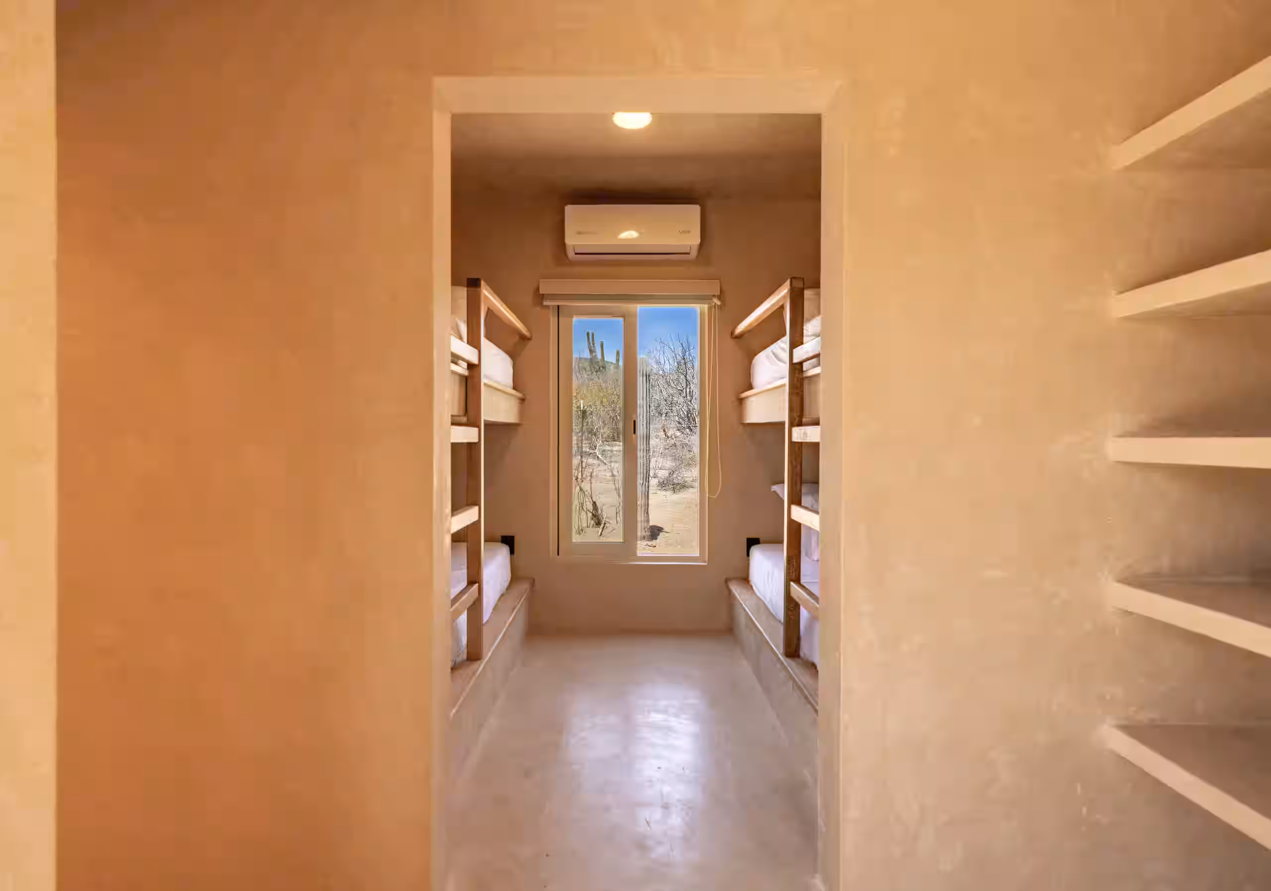 Narrow room with bunk beds and a window view of desert landscape.